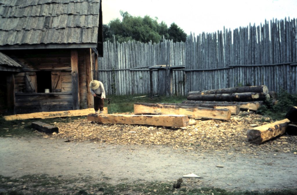 Craftsman using adze to square beams at Sainte-Marie among the Hurons – traditional timber framing demonstration