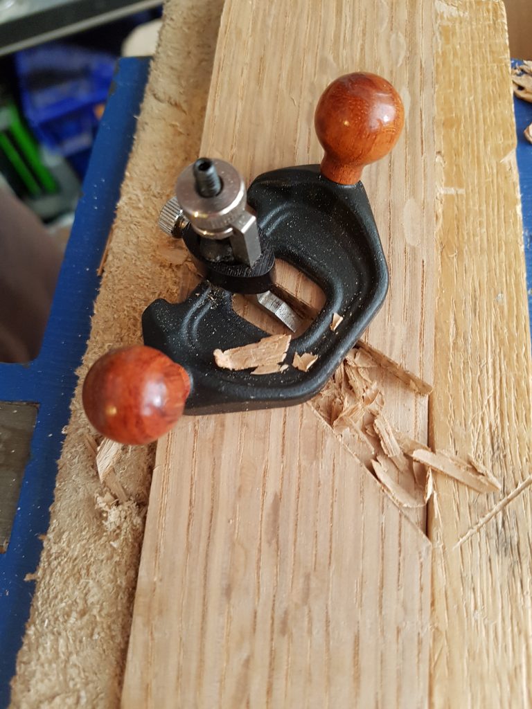 Router plane in use on wooden workpiece – traditional hand tool for flattening grooves to precise depth