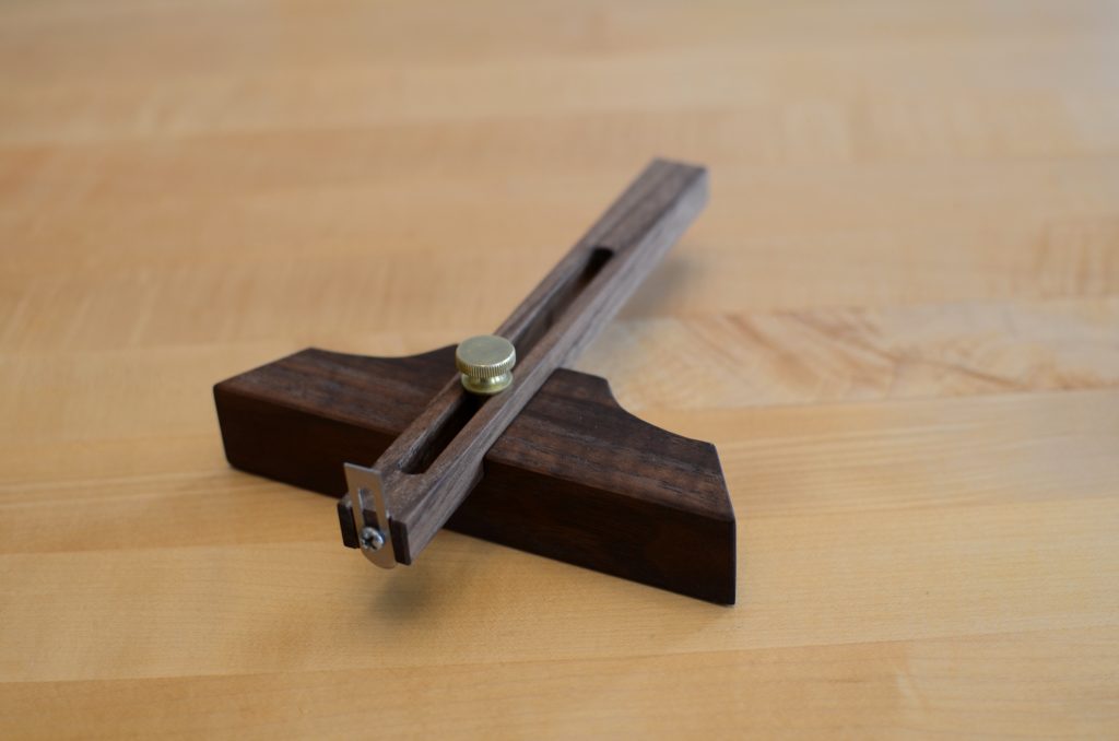 Marking gauge in use, wooden beam with adjustable fence and scribing pin